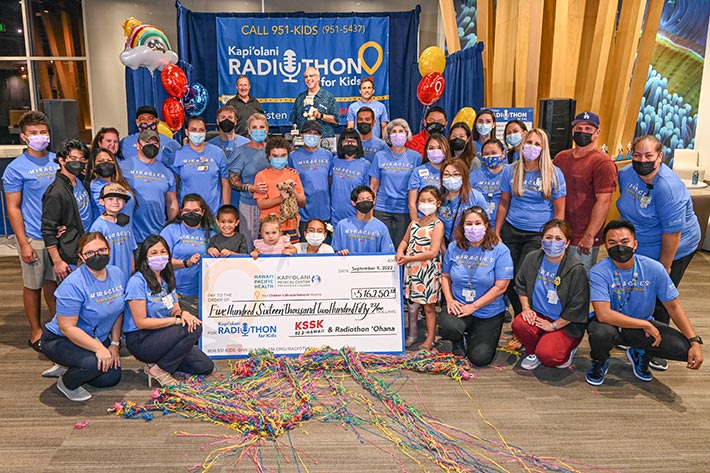 Group of people gathered in front of the Radiothon booth with a giant check for over $516.