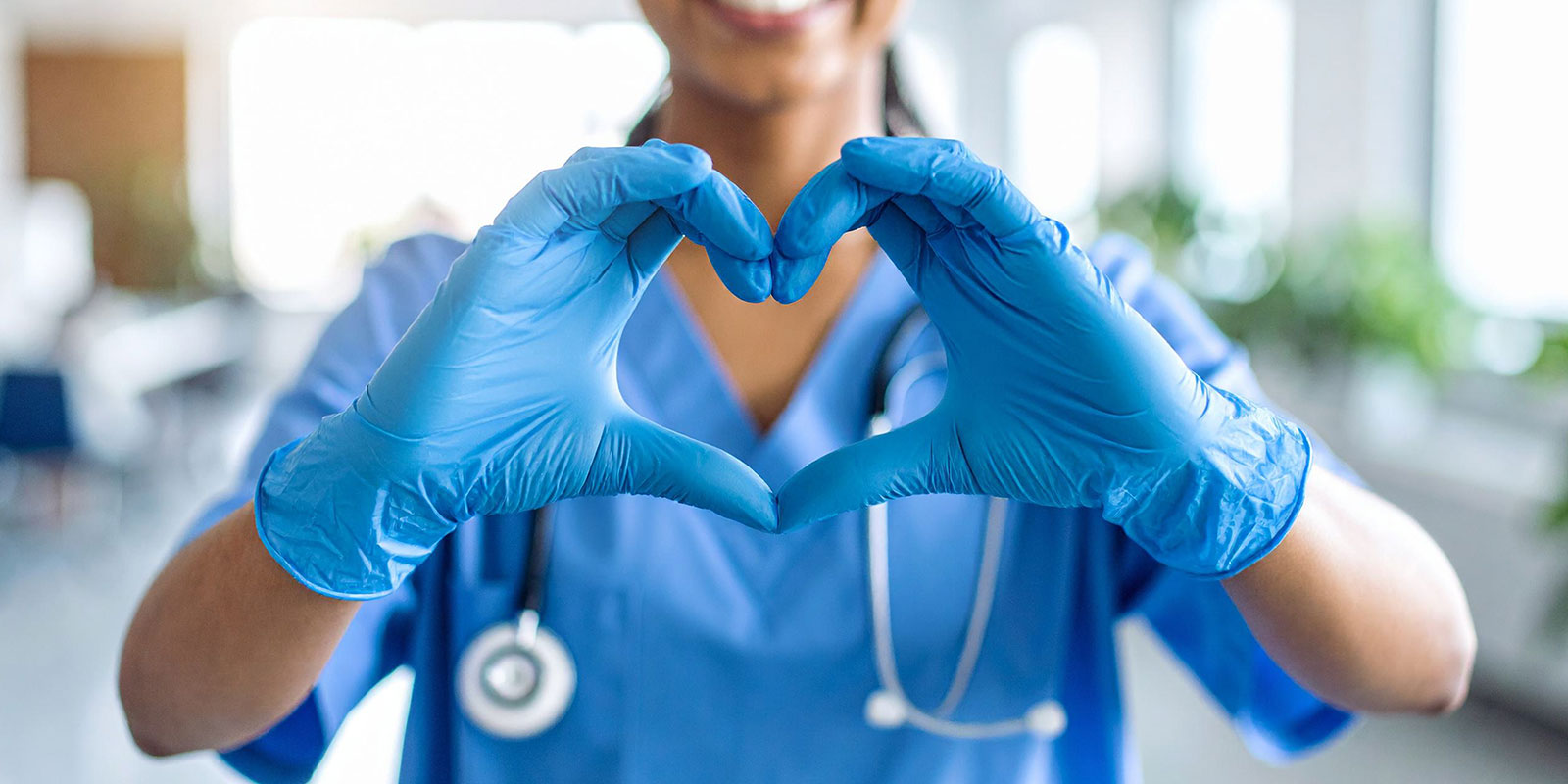 Healthcare working in scrubs wearing latex gloves making a hand heart.