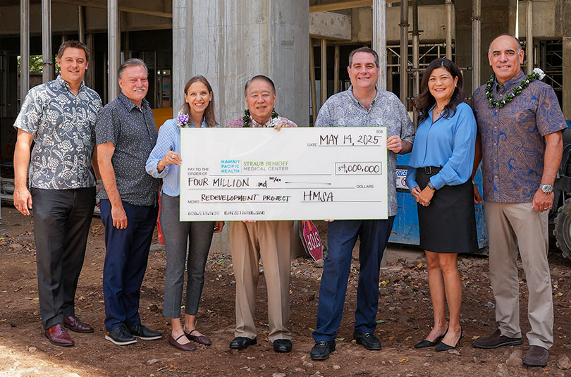 Group of seven people standing in front of a construction site with a giant check for $4 million.