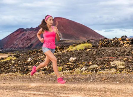 A young woman runs along a rugged path near a hill.