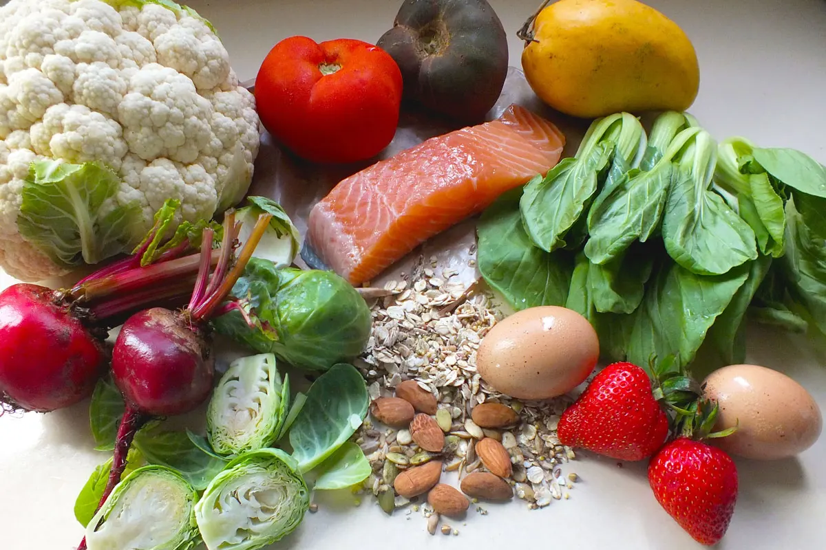 A variety of healthy food, including greens, vegetables, fruits, seeds, nuts, and grains.