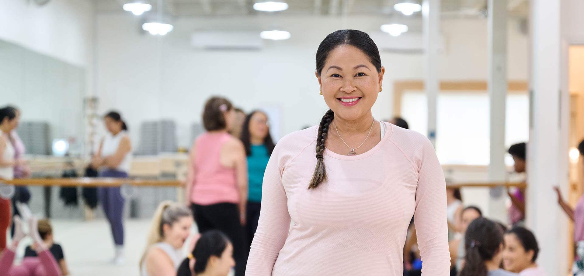 A woman at an exercise class smiles at the camera as other women mingle behind her.