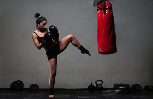 A female kick boxer raises her leg toward a bag.