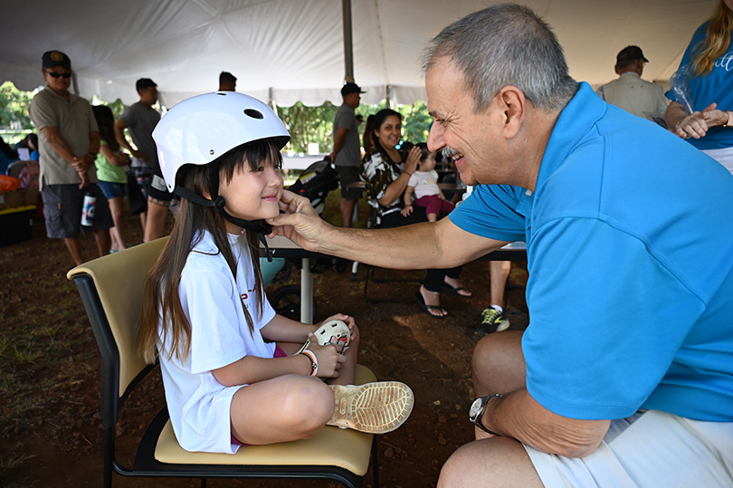 Volunteer helping a young child adjust the strap on her helmet.