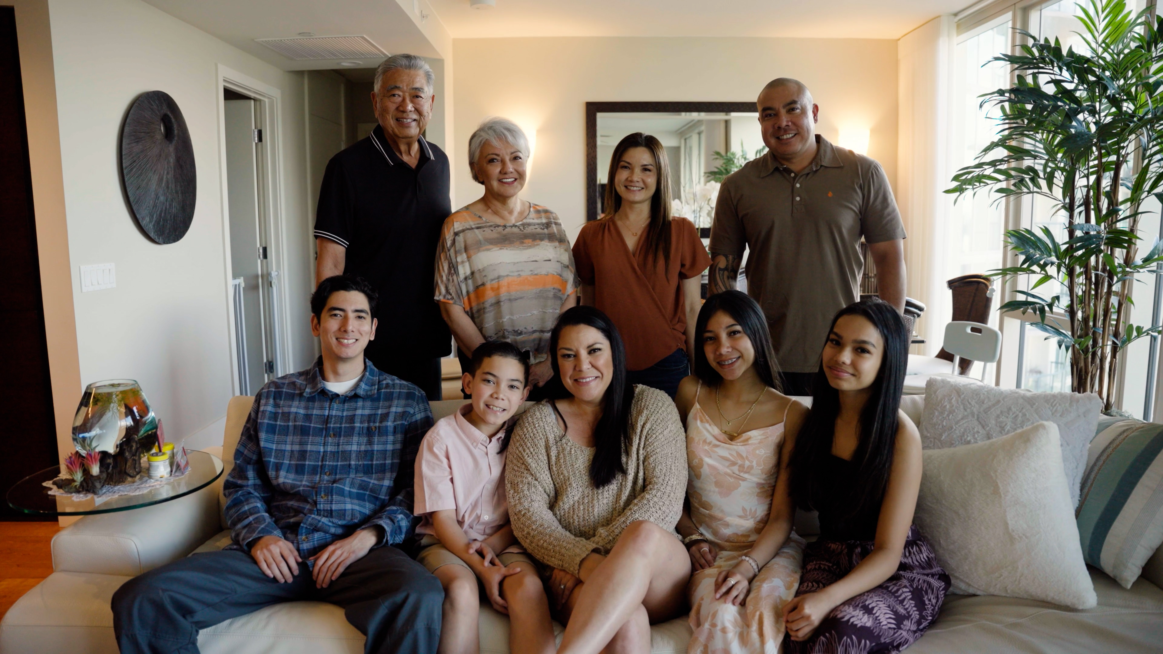 Female patient surrounded by eight loved ones for a family photo in the living room. Everyone is smiling.