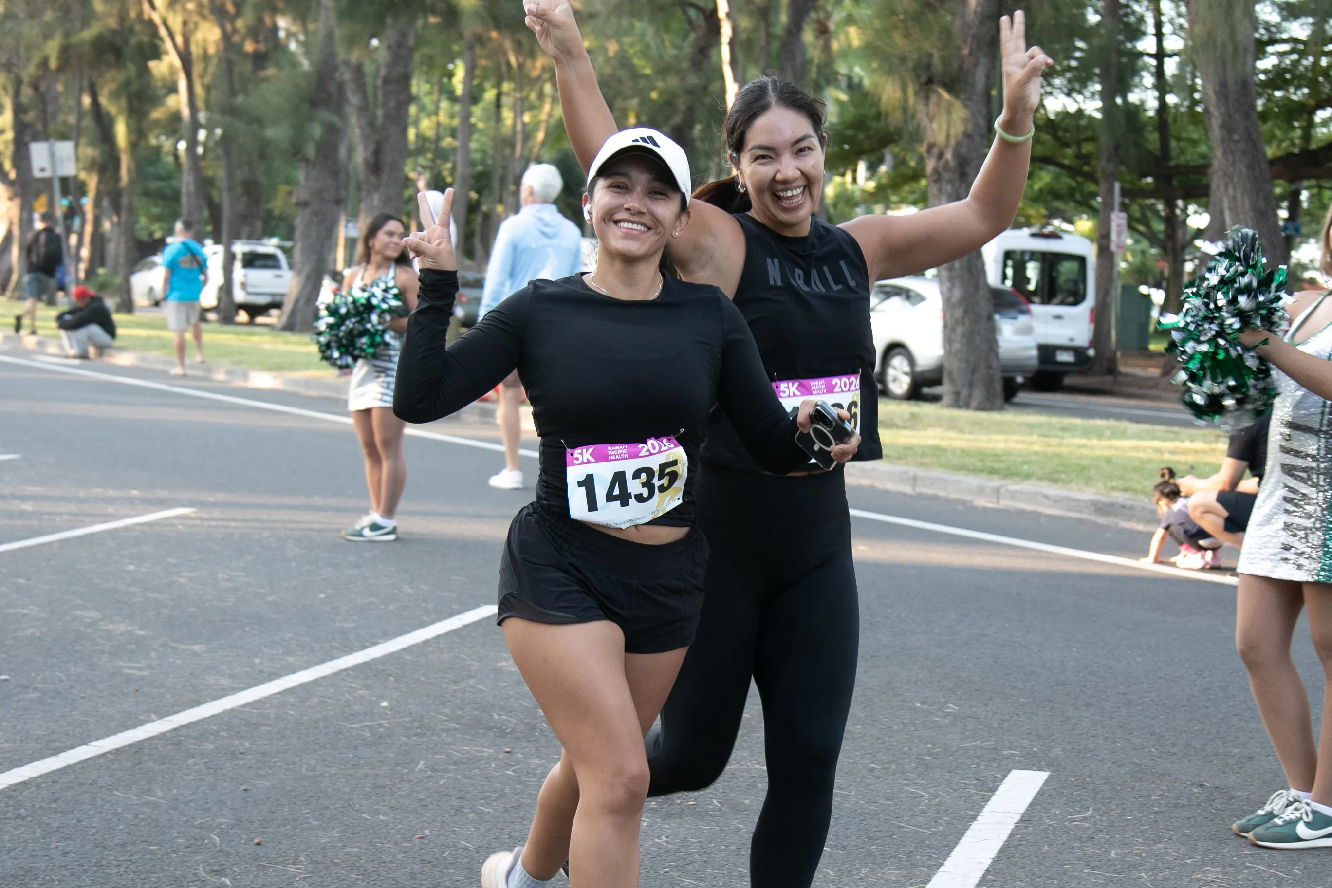 Two 5K runners smiling as they pass the University of Hawaii Rainbow Dancers.