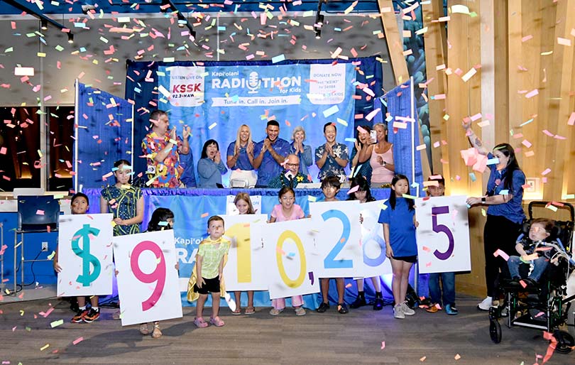 Children cheerfully holding numbers showing $910,285 with confetti falling down and adults cheering.