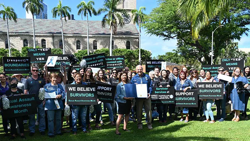 Honolulu Mayor Rick Blangiardi holds the Denim Day proclamation in a crowd of sign-waving supporters.