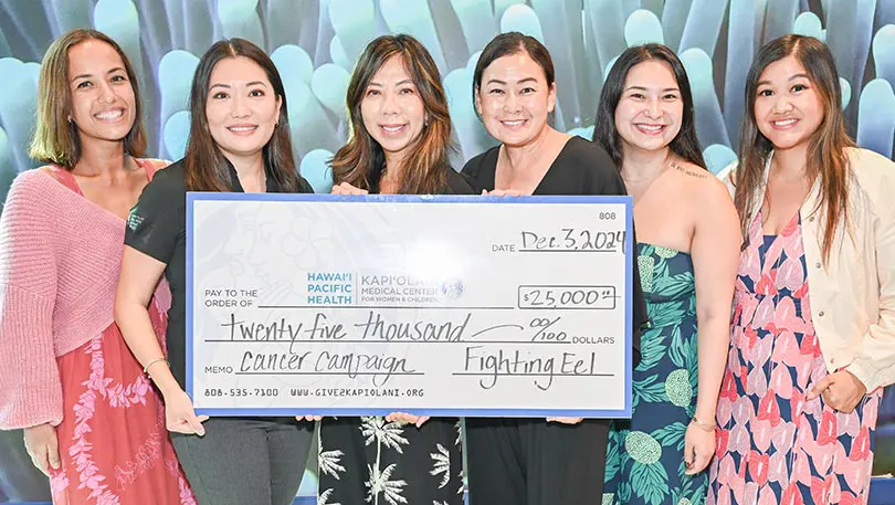 Six women in colorful, floral print outfits holding a giant check for $25,000.