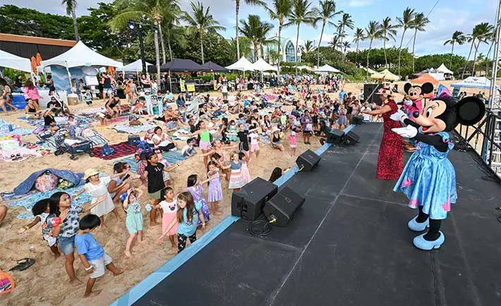 Disney character actors on stage teaching children to dance hula on the beach.  