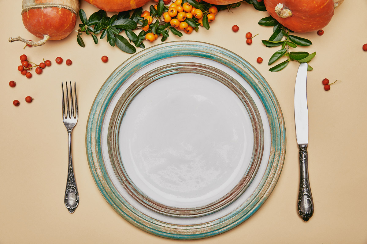 Top view of thanksgiving table set with a plate, fork and knife and decorated with pumpkins and cranberries.