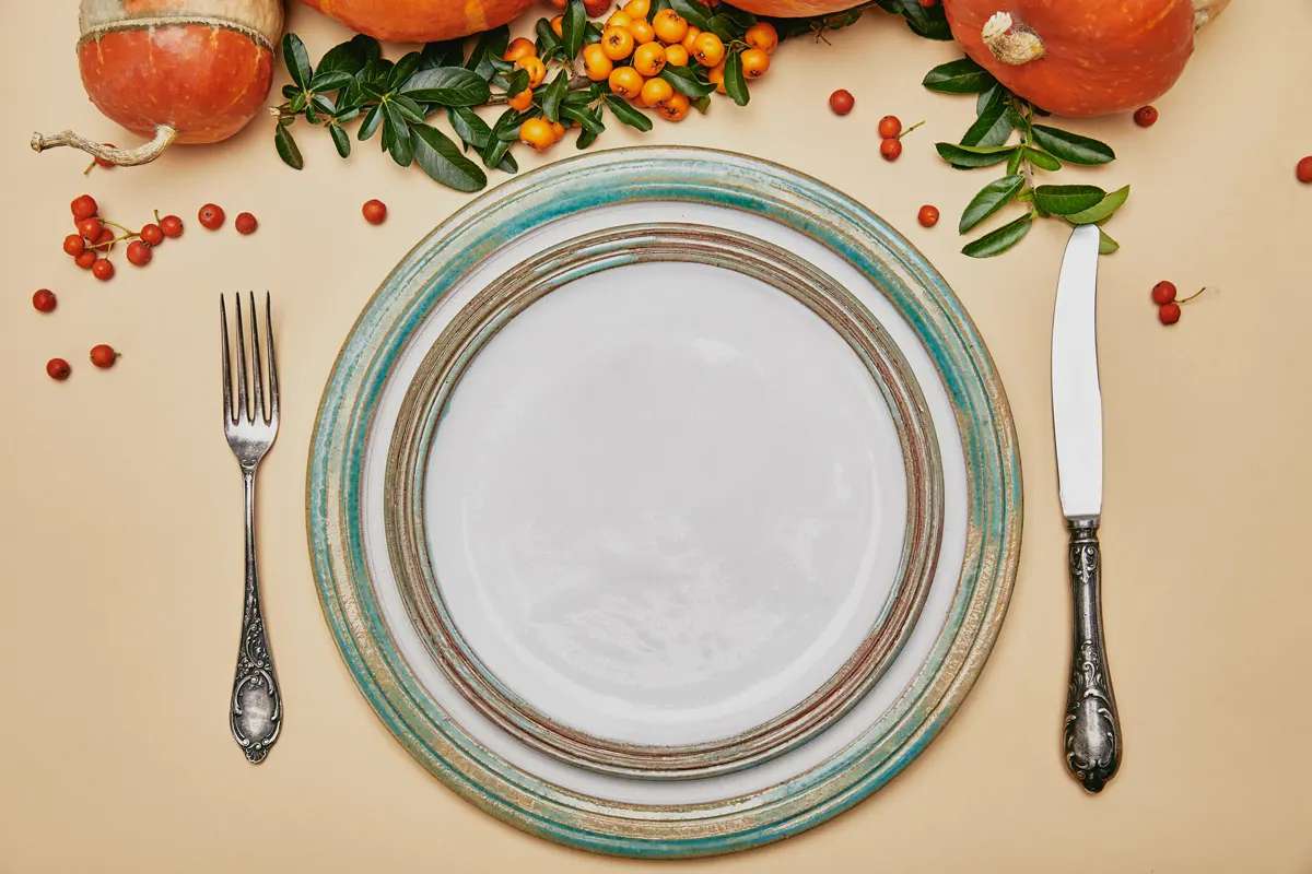 Top view of thanksgiving table set with a plate, fork and knife and decorated with pumpkins and cranberries.