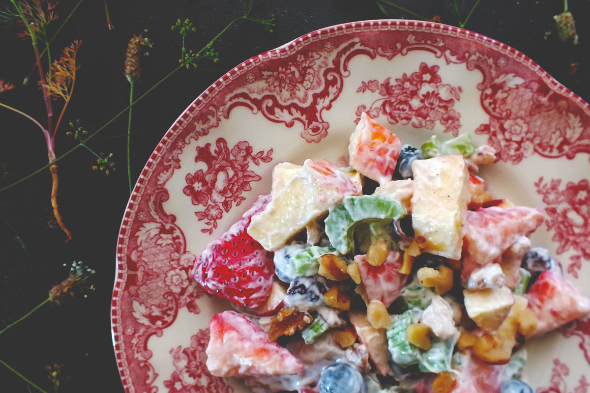 Colorful and creamy, a salad of fruits and vegetables sits on a pink and white dish.