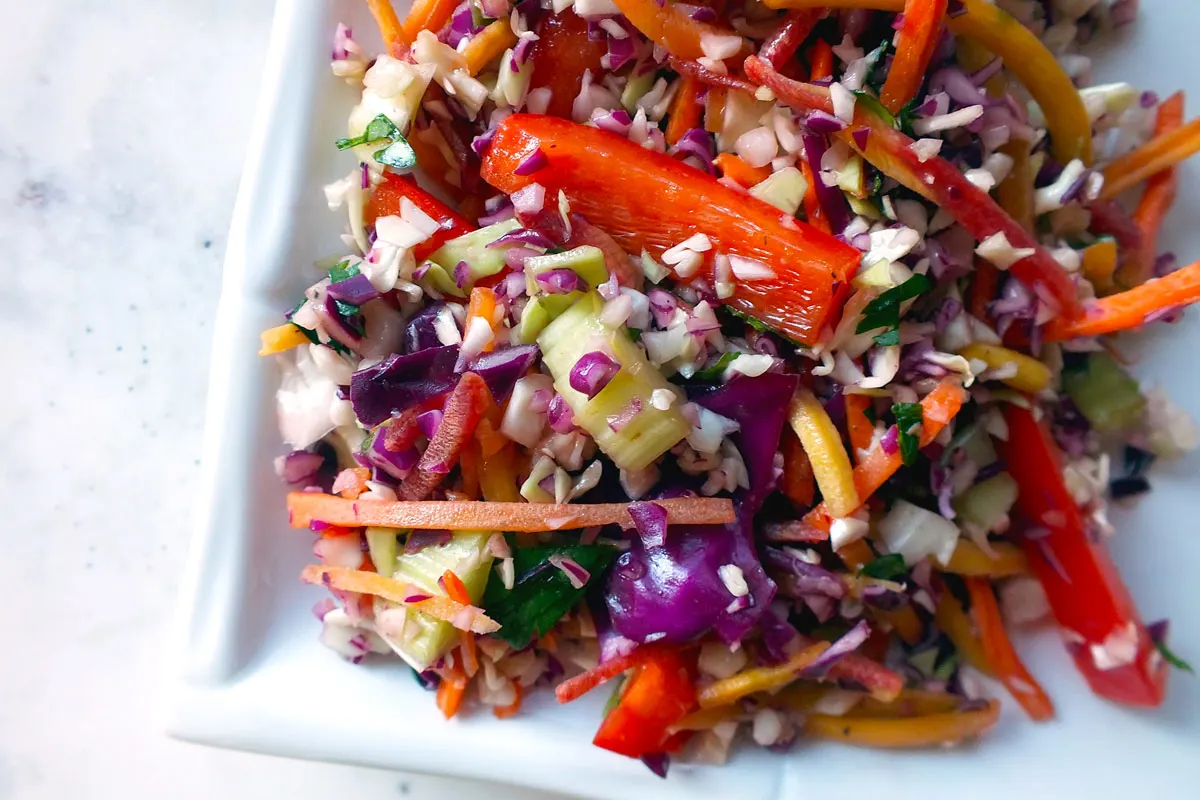 Purple cabbage, red peppers and many other brightly colored veggies mix on a white square plate.