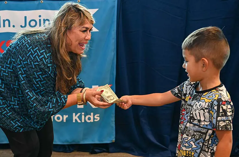 Young boy handing his in-person Radiothon donation to radio personality Sweetie Pacarro.  