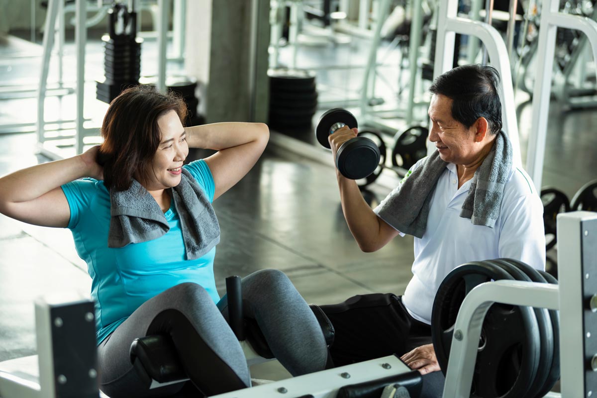 An older woman and man lifting weights and working out together in a gym.