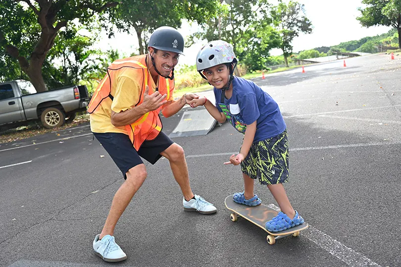Volunteer helping a young child stand on a skateboard.
