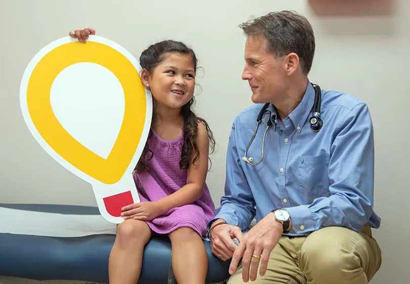 Young patient holding large Children's Miracle Network logo cutout alongside her cardiologist.