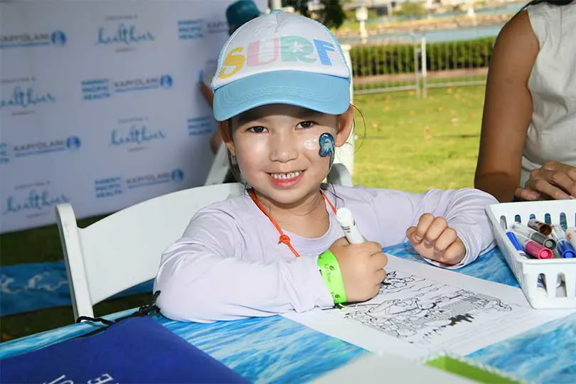 Young girl with face paint smiling while coloring.