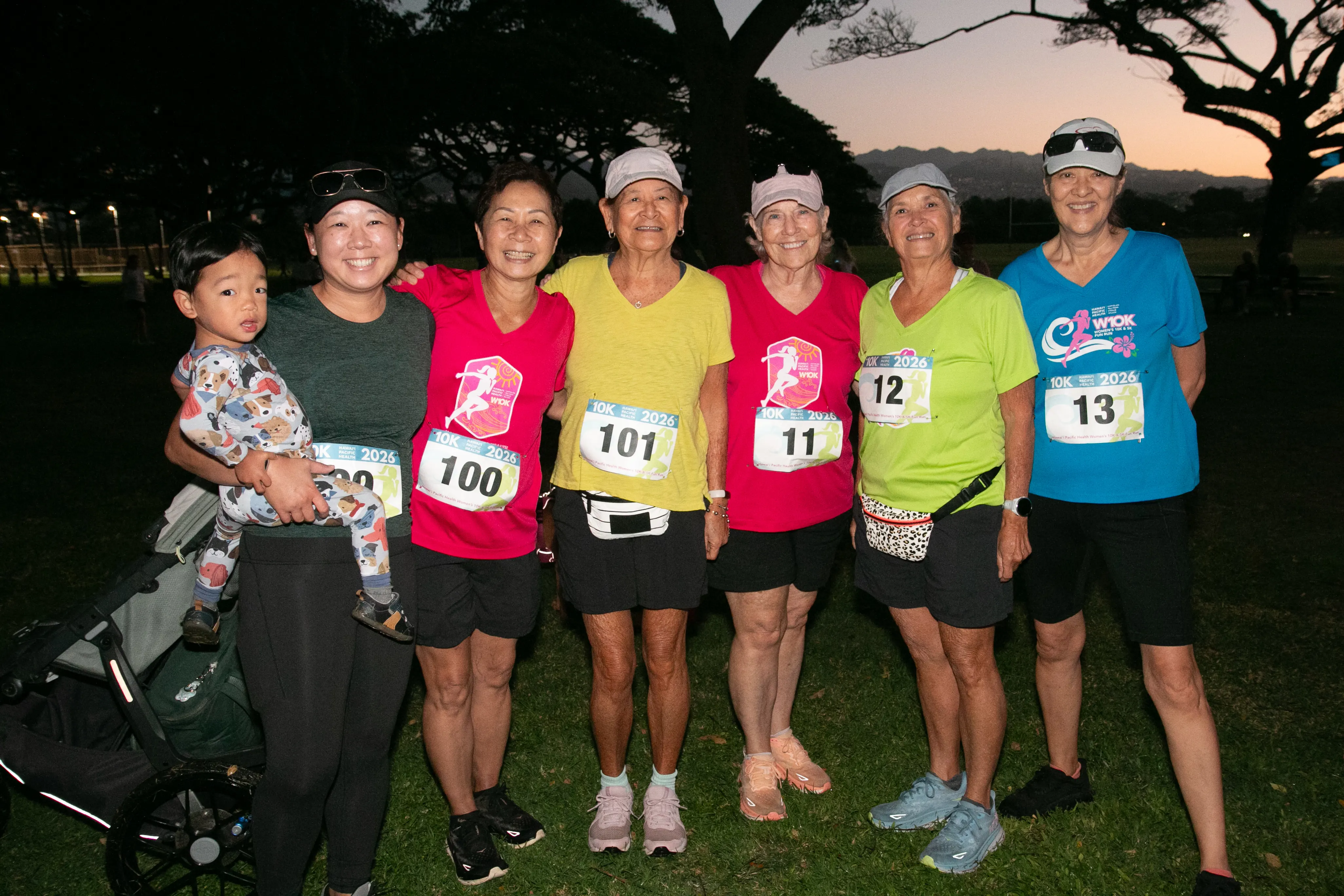 Group of 10K participants headed towards the starting line as the sun rises behind them. One woman is holding a baby.