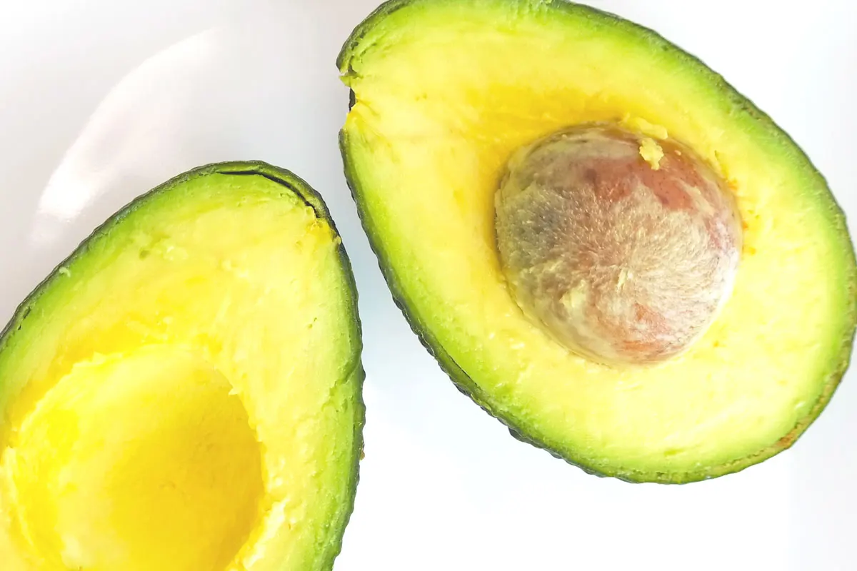 An avocado sliced open with a pit in one half.
