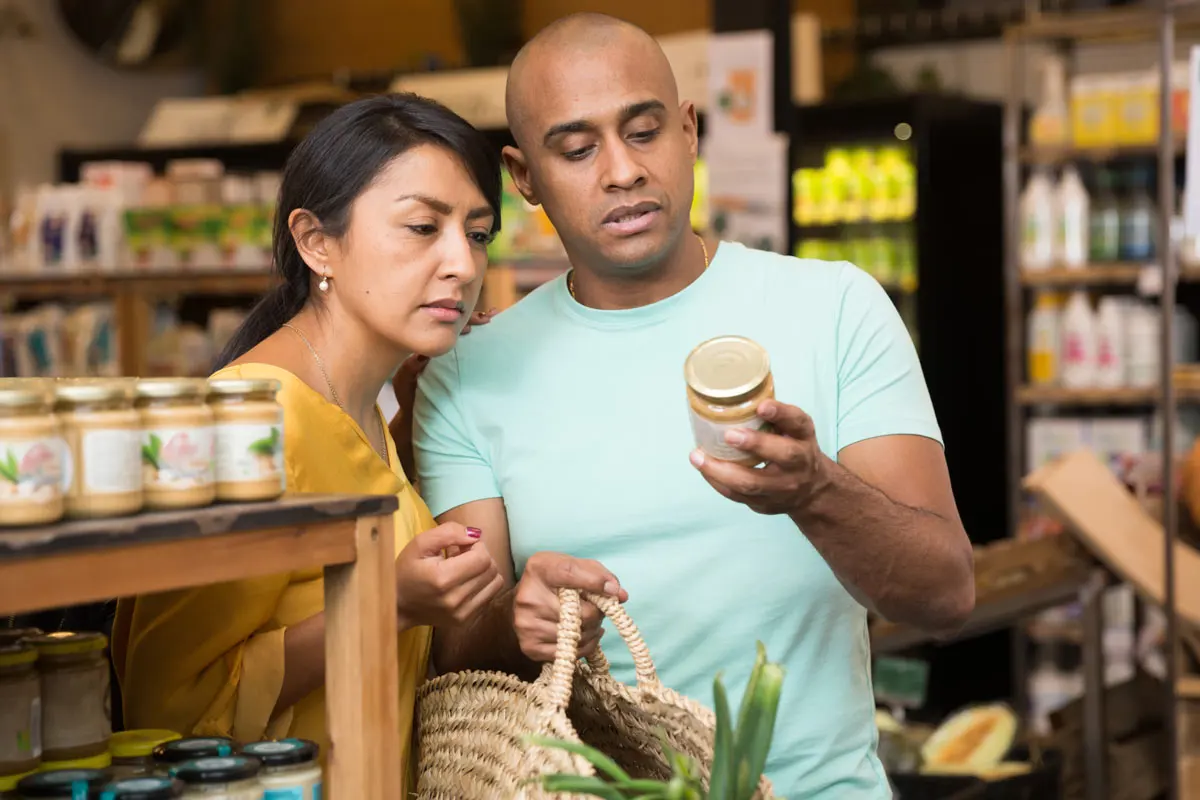 A man and woman look at a label on a jar of honey in a grocery store.