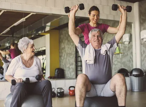A trainer helps an older person with a shoulder press.