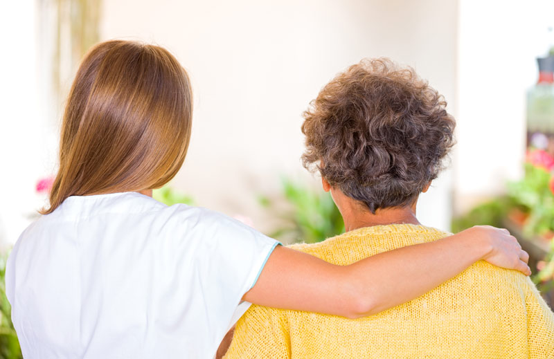 Two people with their back to the camera with one person placing an arm around the other.