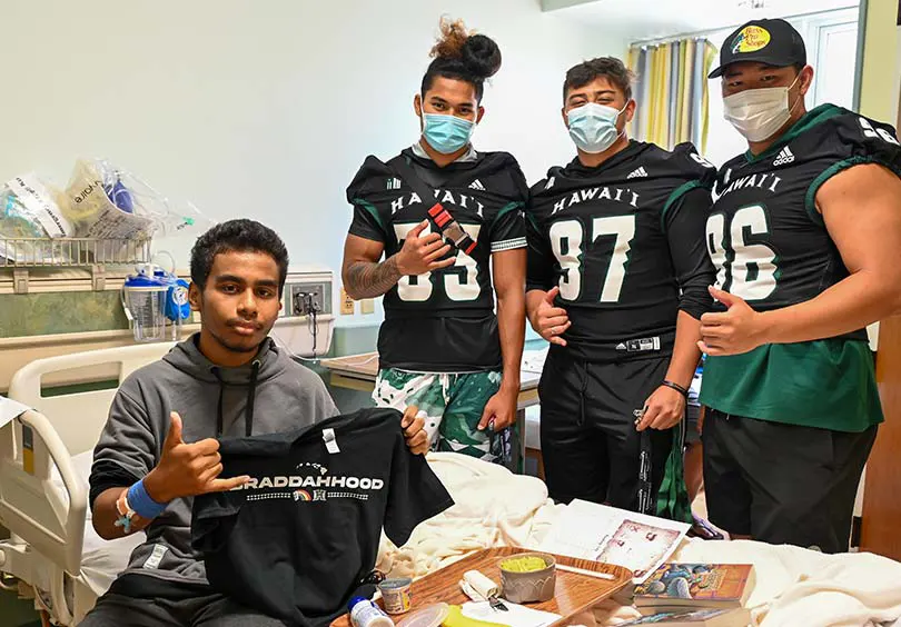 Football players in masks talking with a young male patient at Kapiolani.