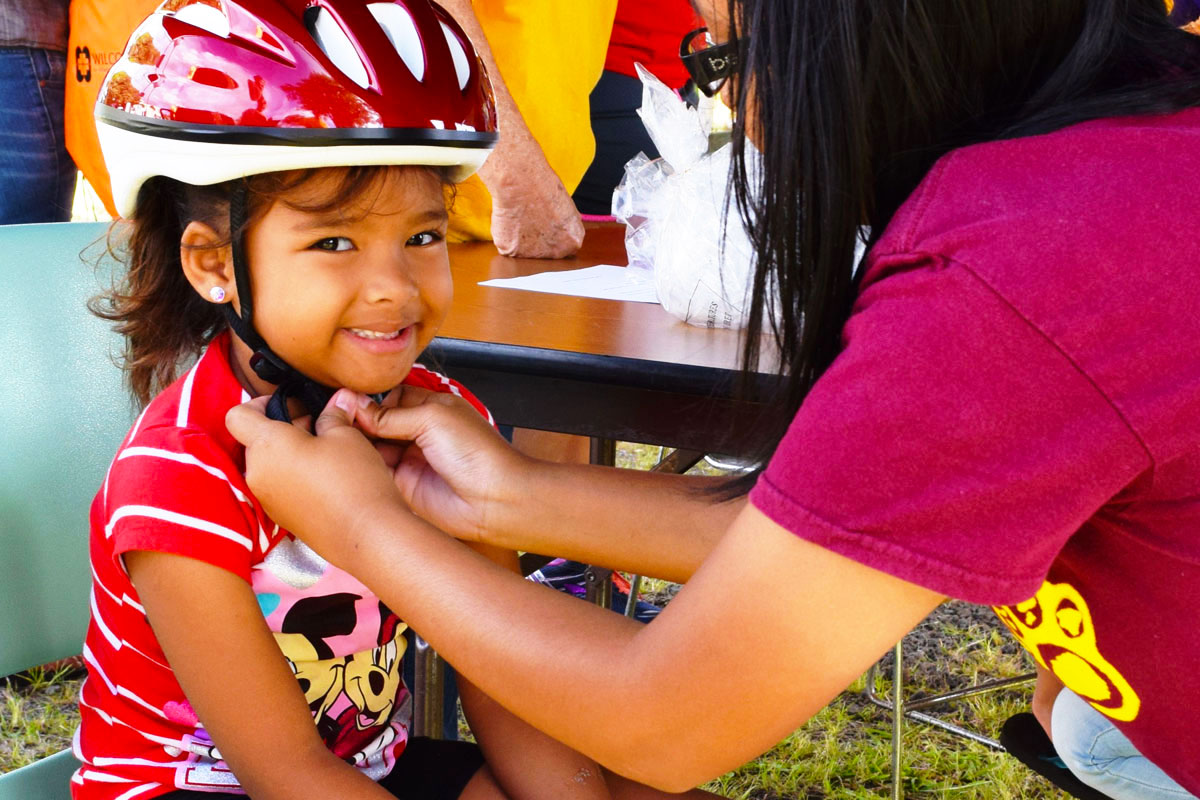 A mother tying bicycle helmet to her child.