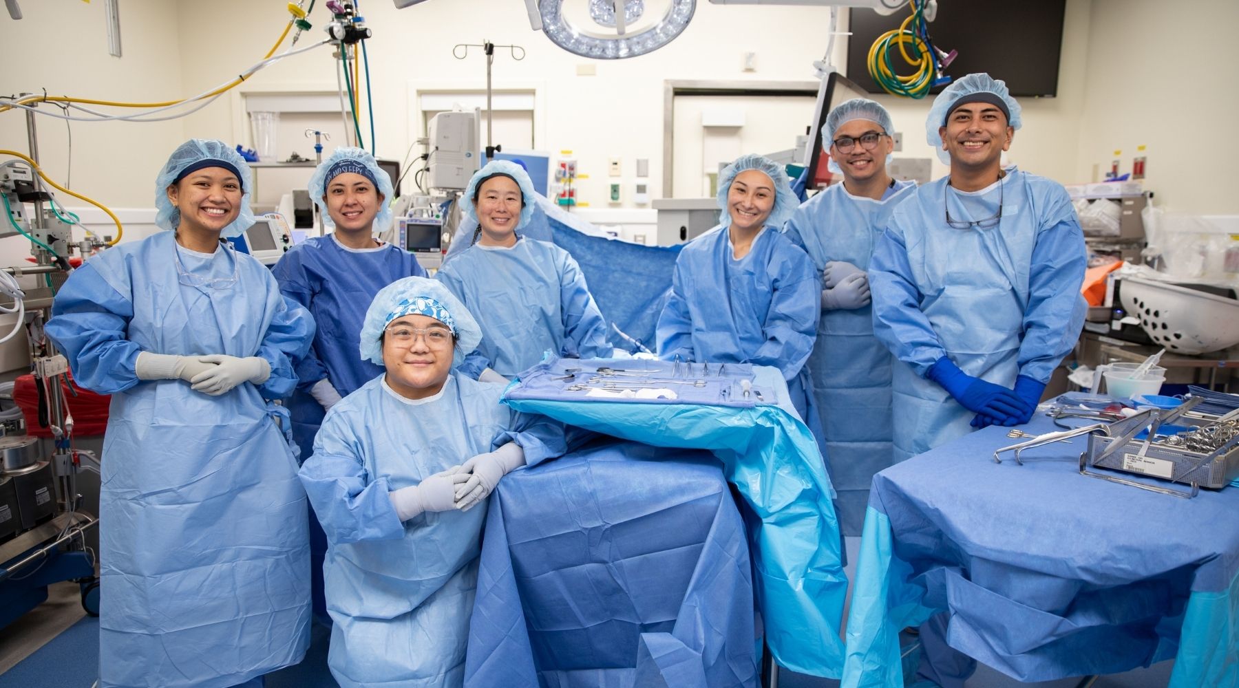Surgical technologist students in scrubs stand together in an operating room with instruments and equipment visible.