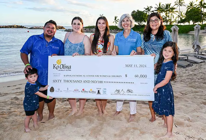 Group of six people standing on the beach and holding a giant check with $60,000 donation amount.