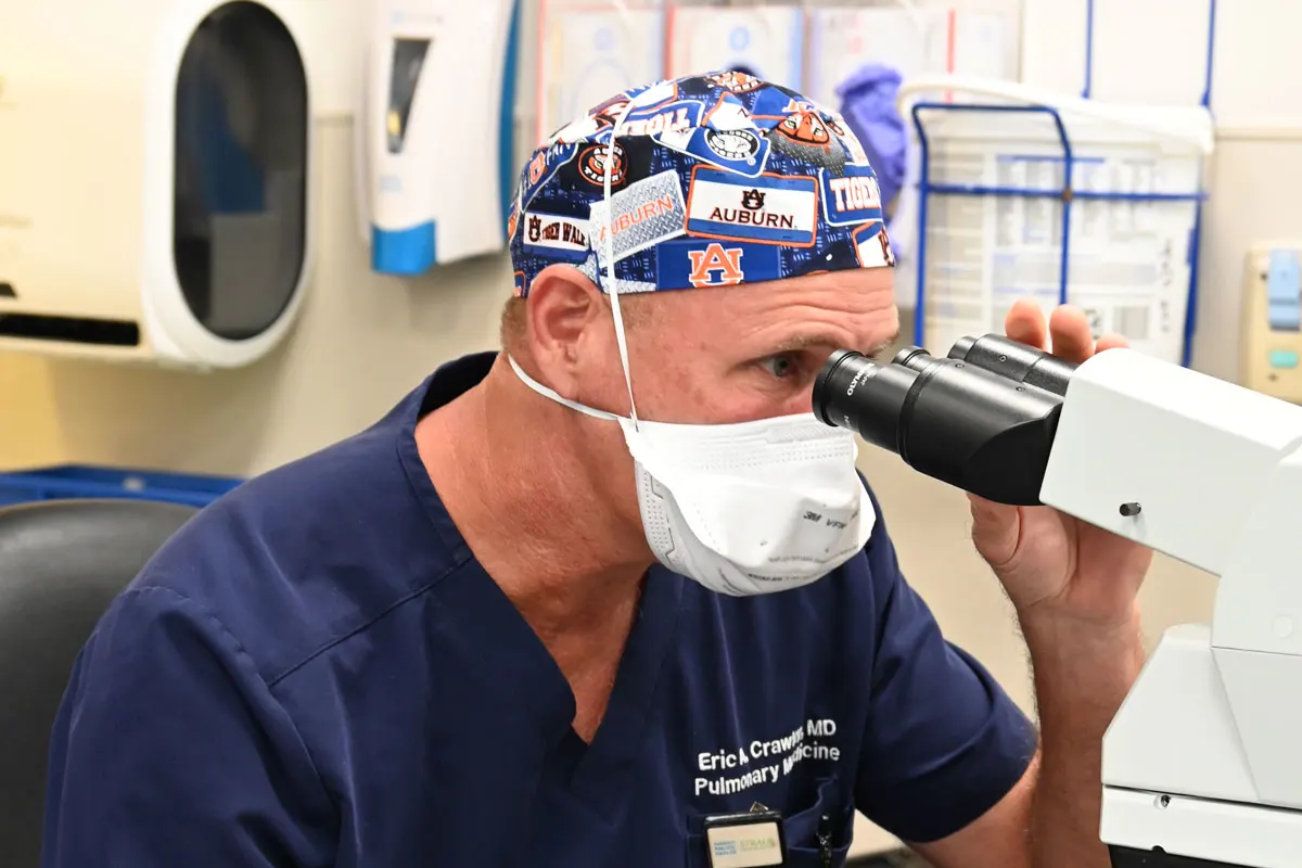 A doctor in scrubs looks into a microscope.