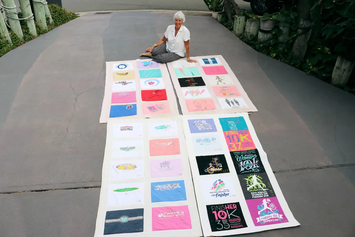 Woman sitting in her driveway with 40 finisher shirts quilted together.