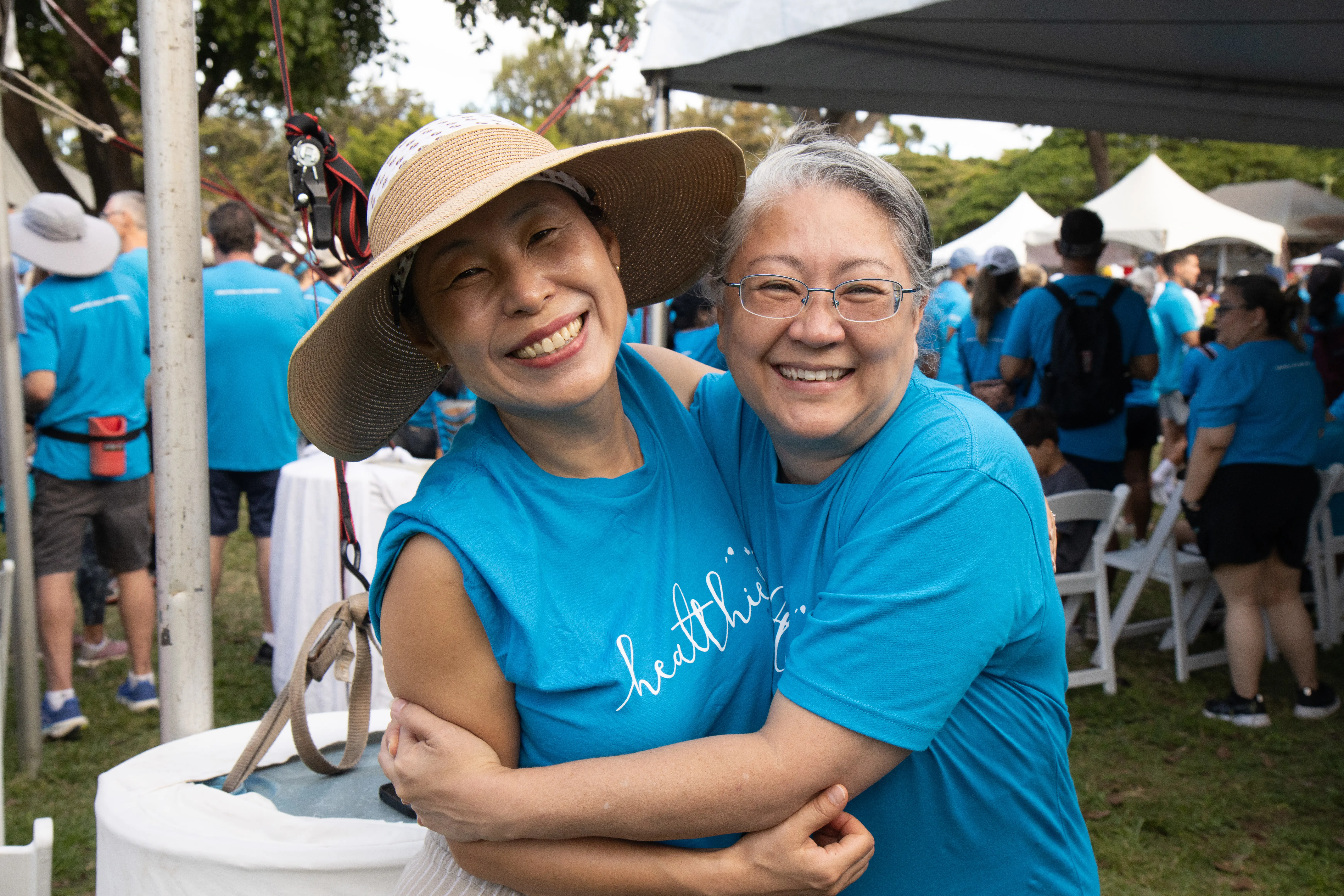 Two women smiling at an outdoor event wearing matching t-shirts.