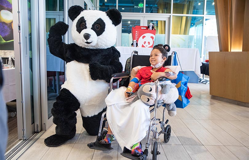 Child posing with someone in a panda mascot suit on the Kapiolani lanai.
