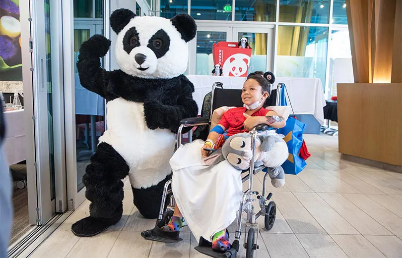 Child posing with someone in a panda mascot suit on the Kapiolani lanai.