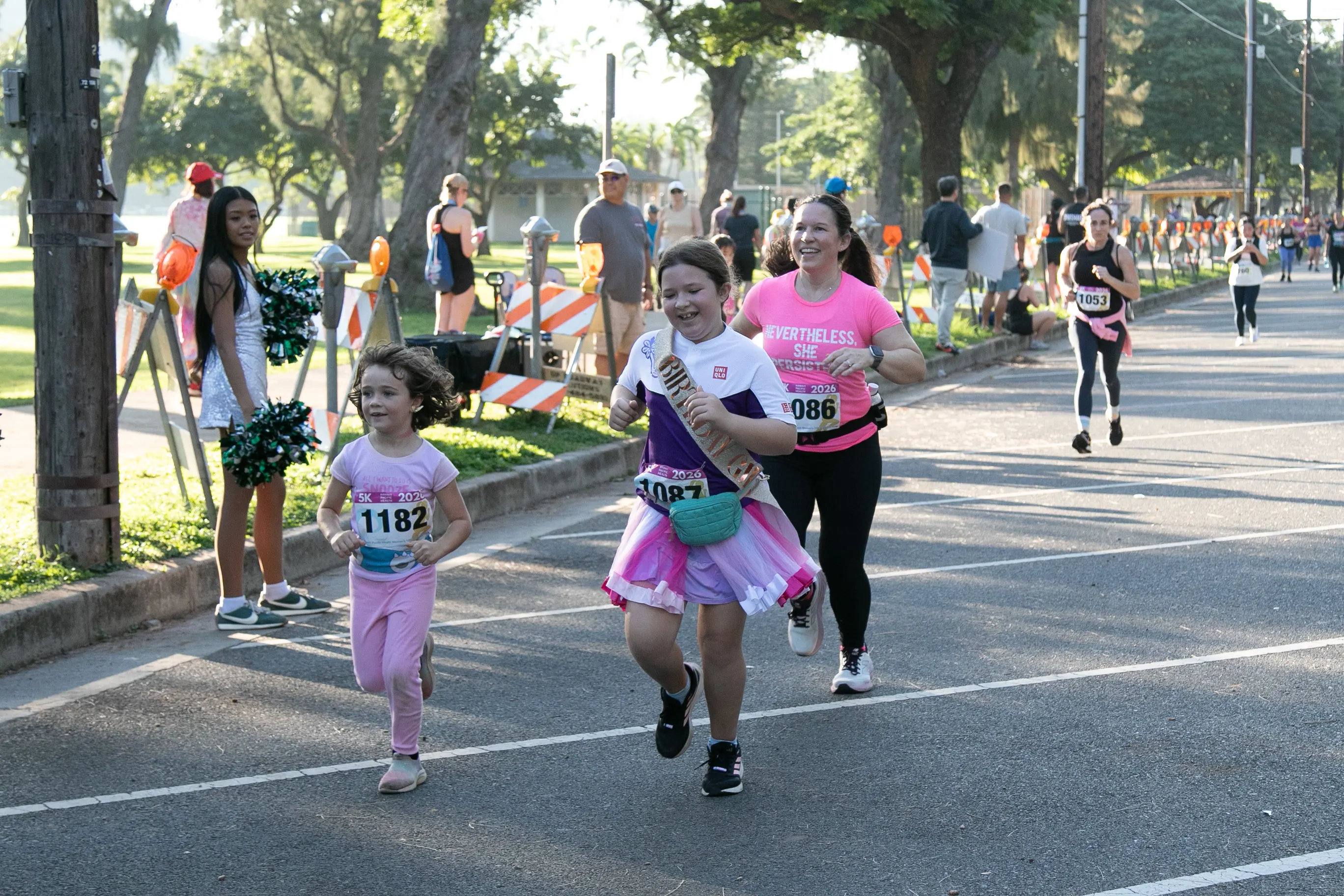 Two sisters cheerfully running the 5K with their mom. One girl is wearing a gold sparkly birthday sash. 