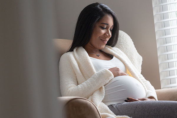 Pregnant woman smiling, looking down and holding her belly.