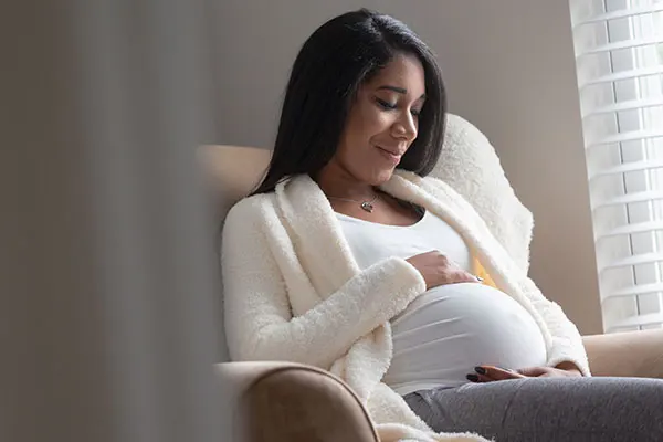 Pregnant woman smiling, looking down and holding her belly.
