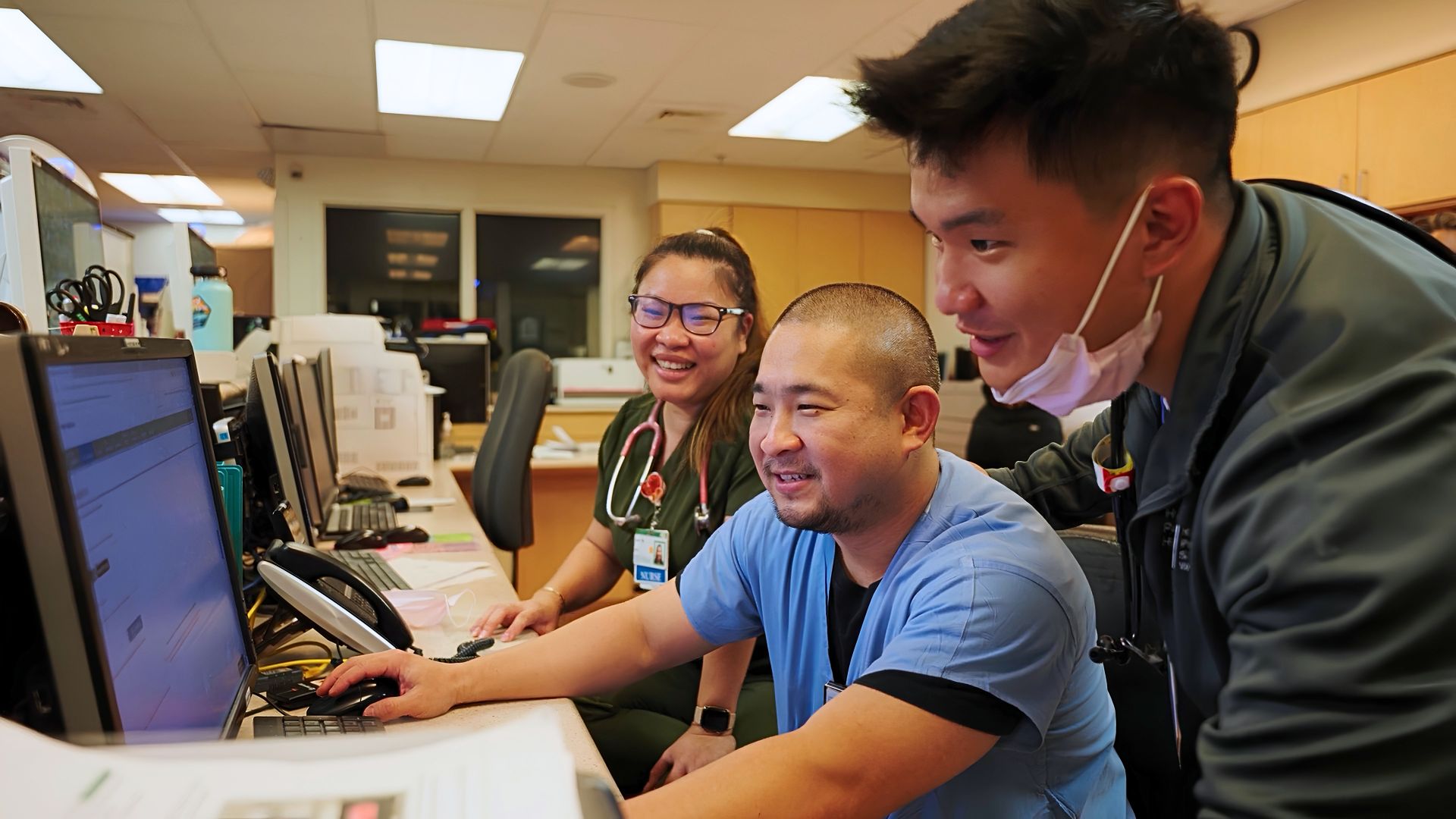 Three healthcare workers review information together on a computer at a nurses’ station.