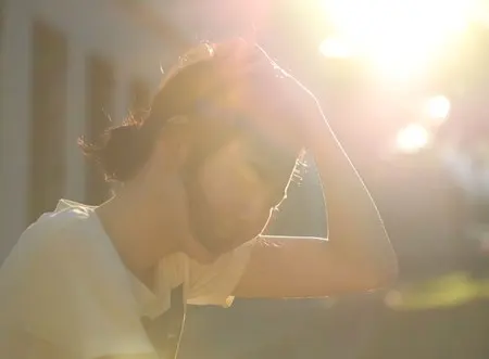 A person with their hand on their head in bright sun.