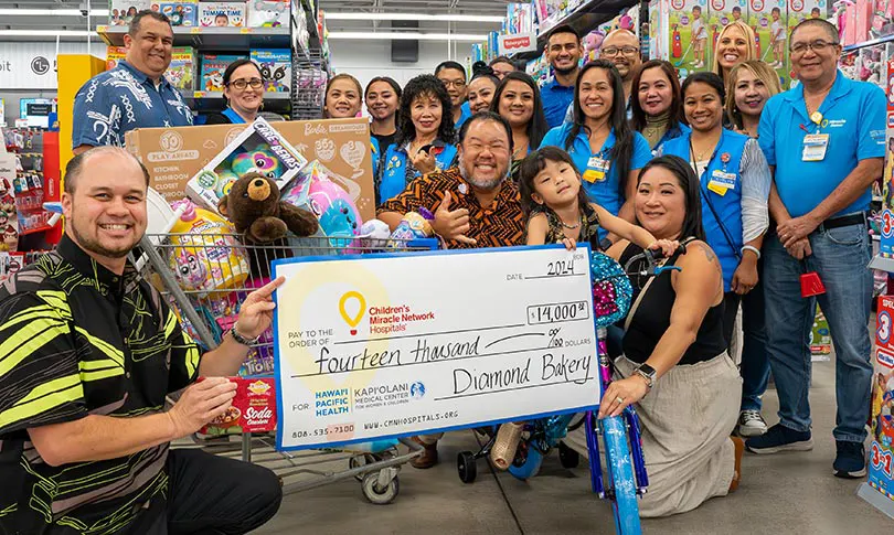 A group of Walmart employees cheerfully supporting Diamond Bakery leadership presenting a giant check for $14,000 in the Walmart toy section with a shopping cart full of toys.