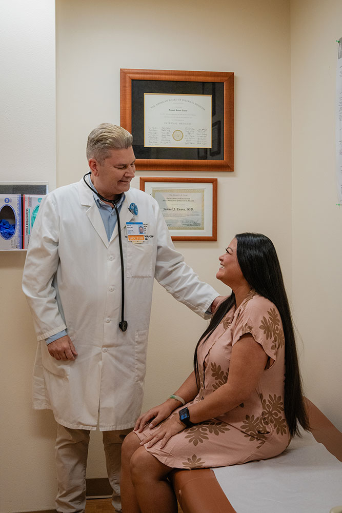 Doctor in white coat standing next to a patient seated in an exam room.