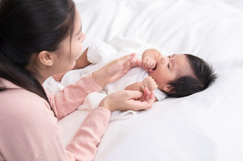 Woman over her infant child laying on a large bed.