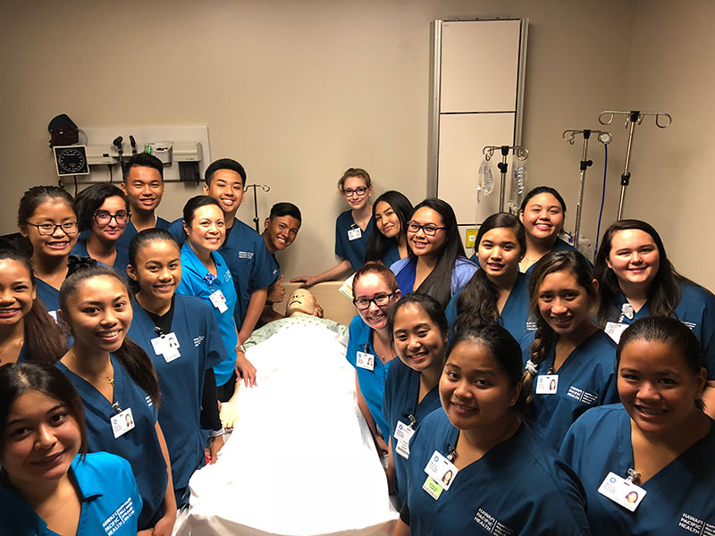 Group shot of high school students in scrubs with patient simulator dummy.