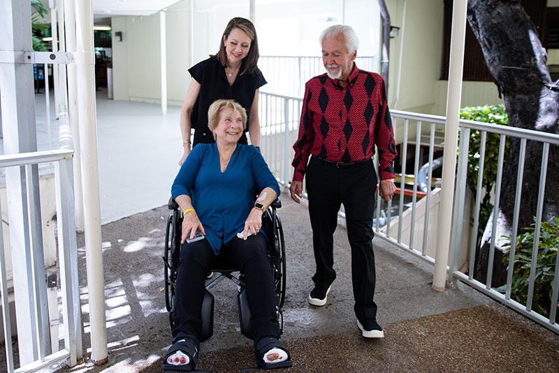 Two people accompany a patient in a wheel chair. 