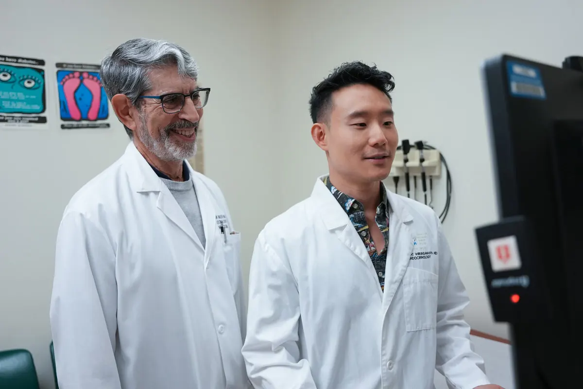 Two male doctors look at a computer screen in an exam room.