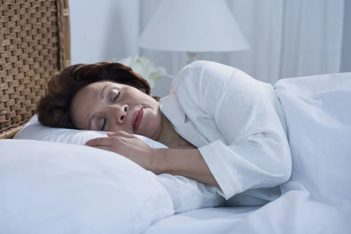 A lady sleeping with her head on a white pillow.