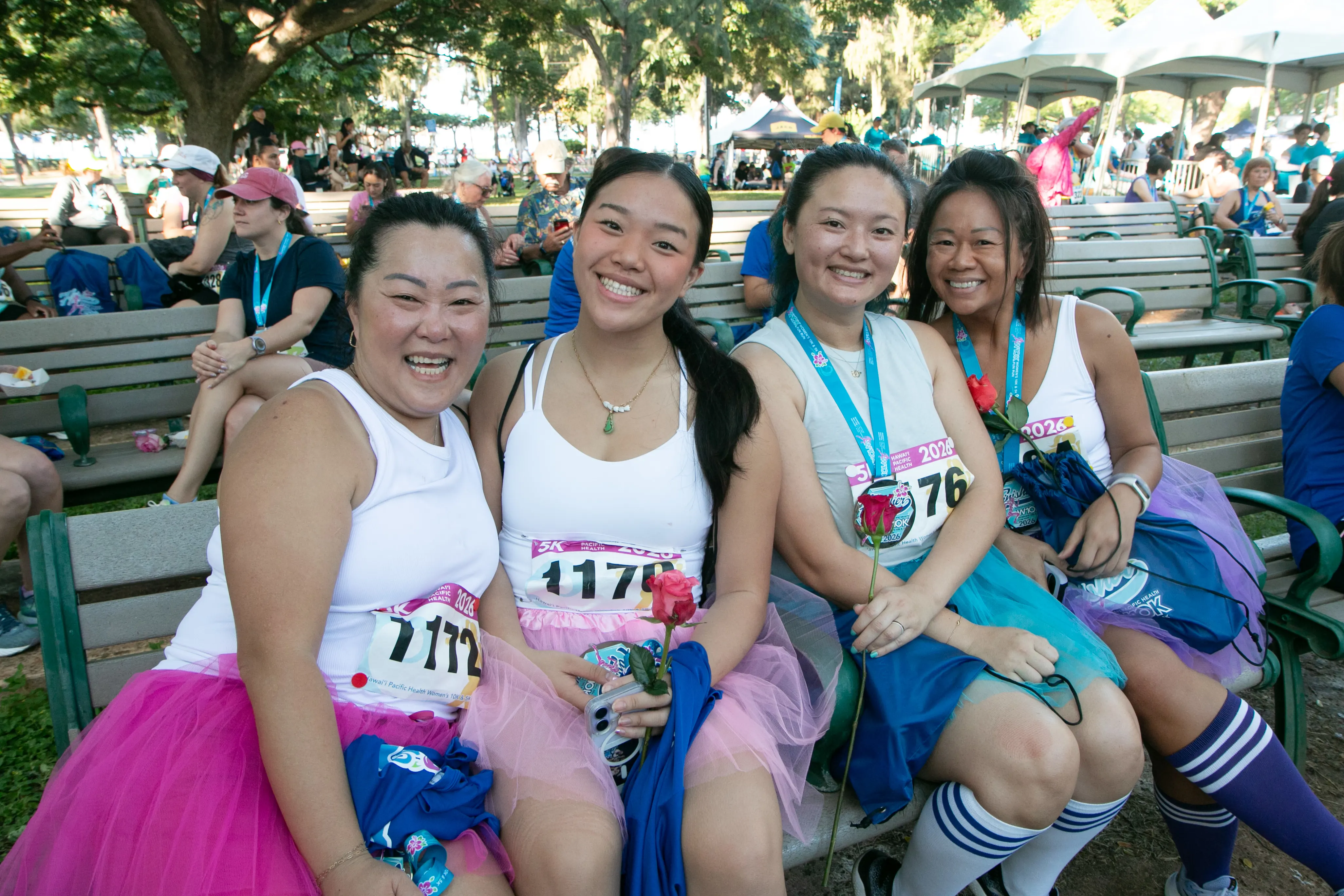 Two mothers in matching outfits with their daughters smiling on the bench.